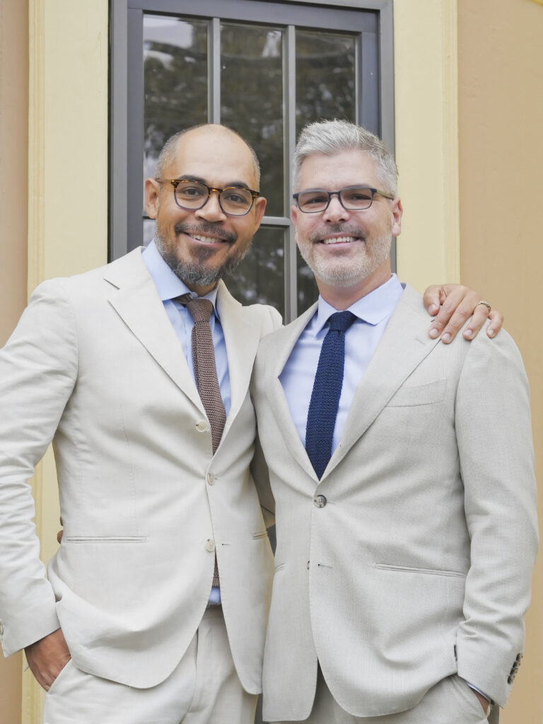 Two grooms in cream and navy suits outside their venue